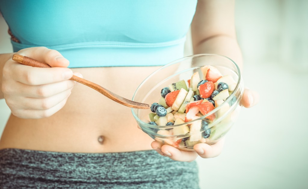 Mulher comendo salada de frutas 5 alimentos cicatrizantes que vão recuperar a sua pele pós-procedimentos