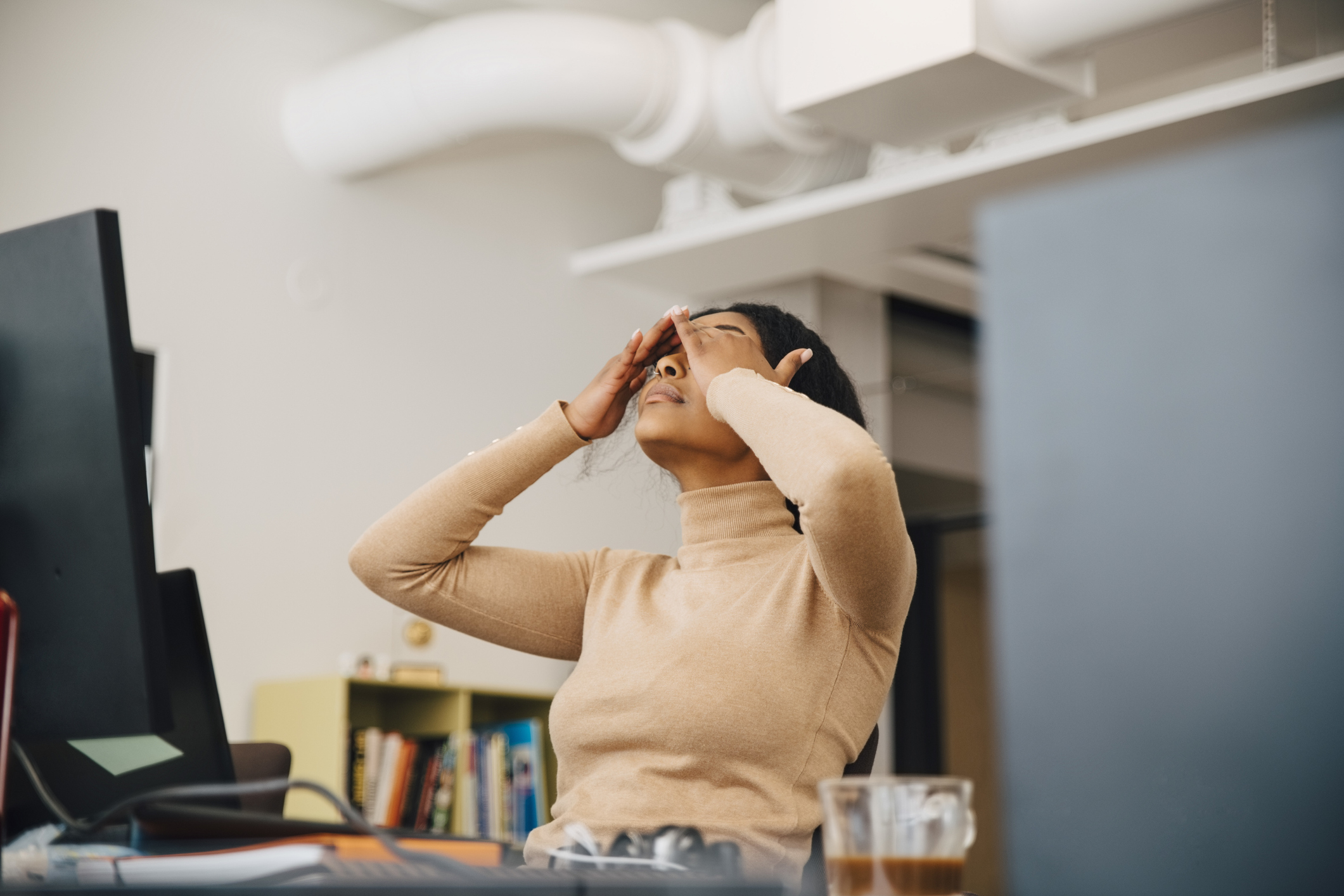 Frustrated female computer programmer with head in hands sitting in creative office -