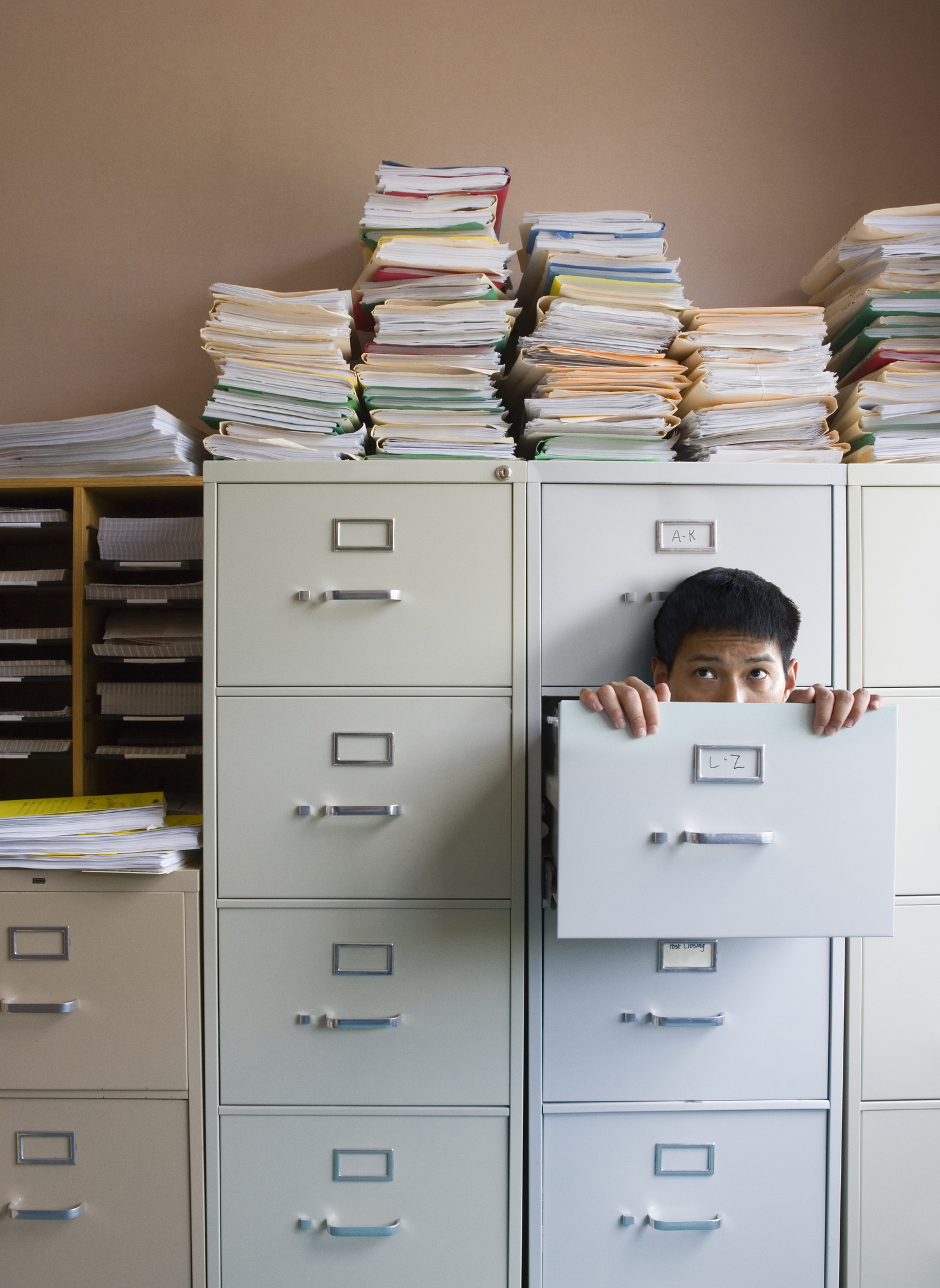 Young man peeking out of drawer in filing cabinet Todos os afazeres a mais que a pandemia criou estão nos fazendo sentir vergonha de não dar conta